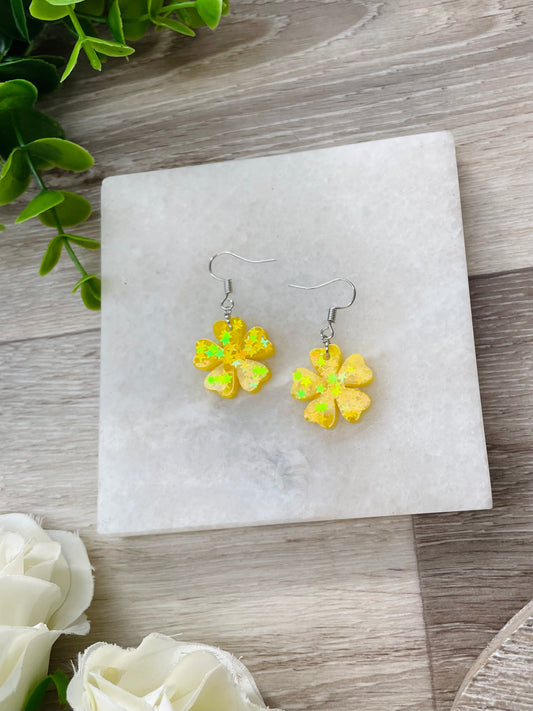 Sunshine yellow mini cranesbill flower earrings on timber background. These earrings are handmade in New Zealand with  epoxy resin.
